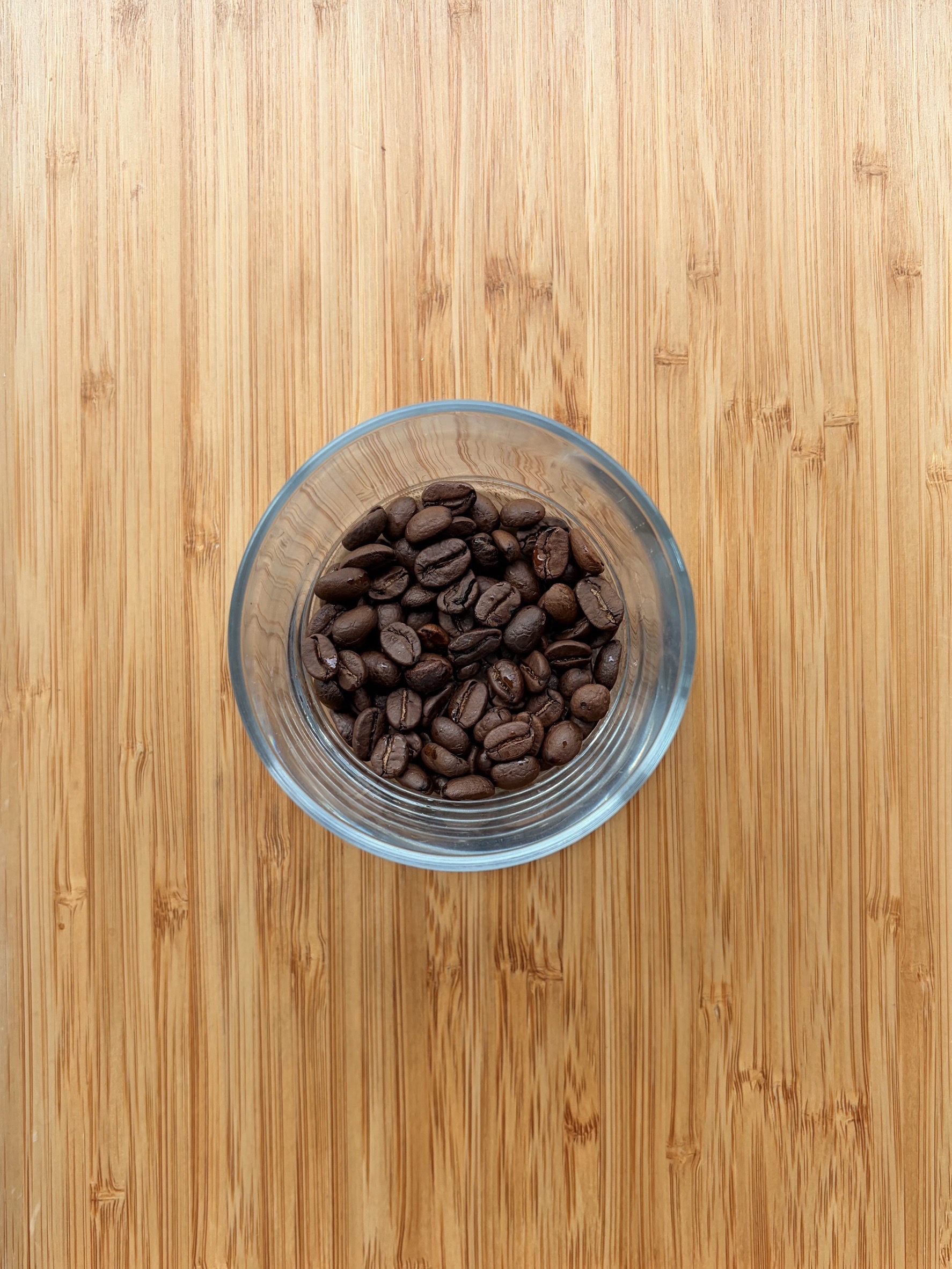 Roasted coffee beans in a glass bowl on bamboo
